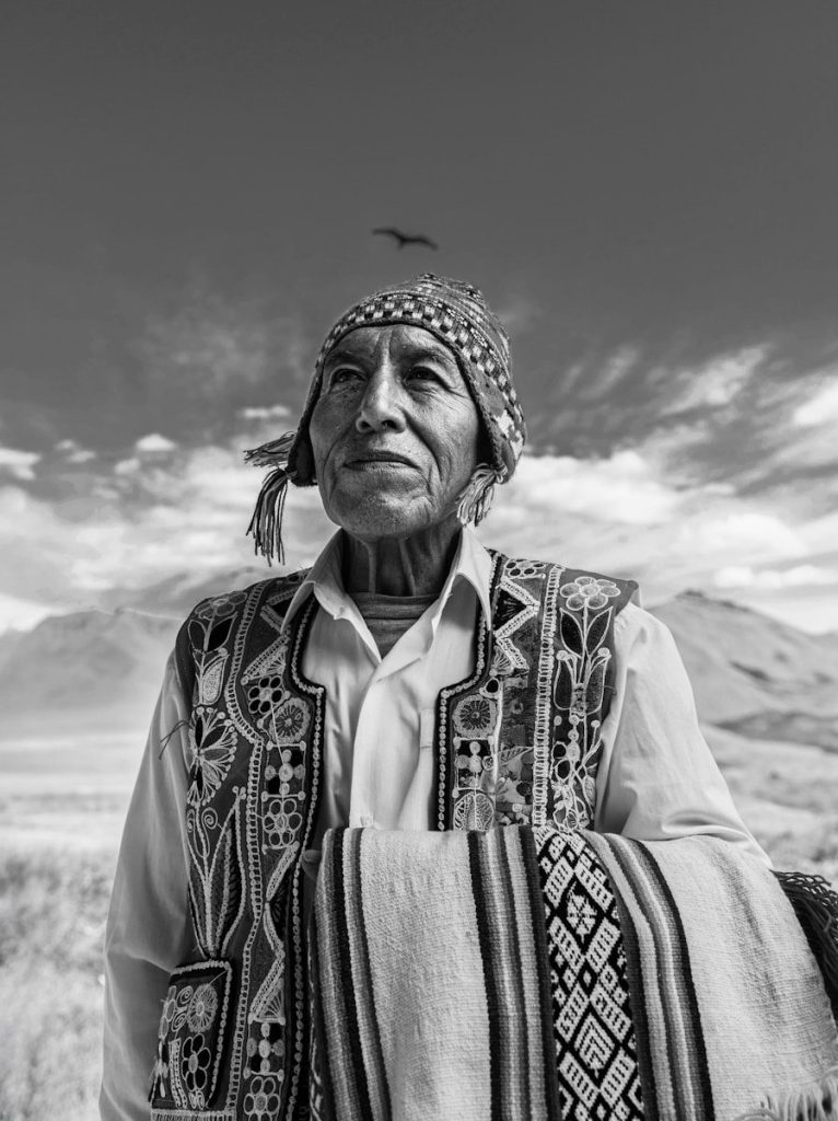 Elderly man in traditional clothing with mountains behind